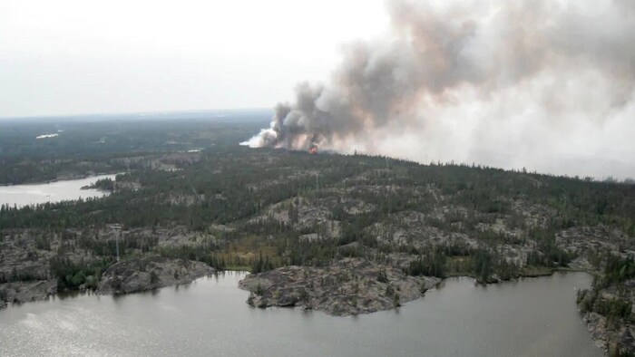 Vue aérienne d'un secteur boisé. Une épaisse fumée et des flammes peuvent être apperçus.