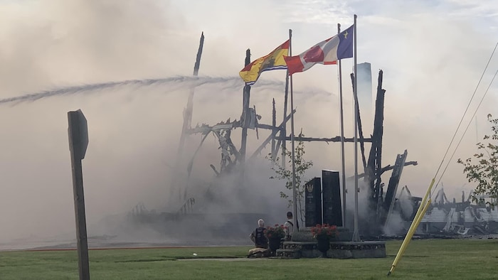 Des pompiers assis, devant ce qui reste de l'église incendiée de Saint-Simon.