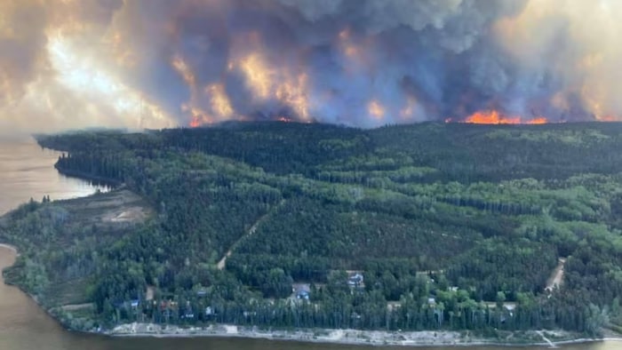 Un feu de forêt se rapproche d'une petite ville au bord de l'eau.