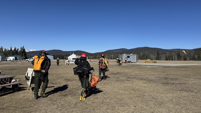 Des pompiers forestiers équipés de sacs à dos marchent vers un hélicoptère.