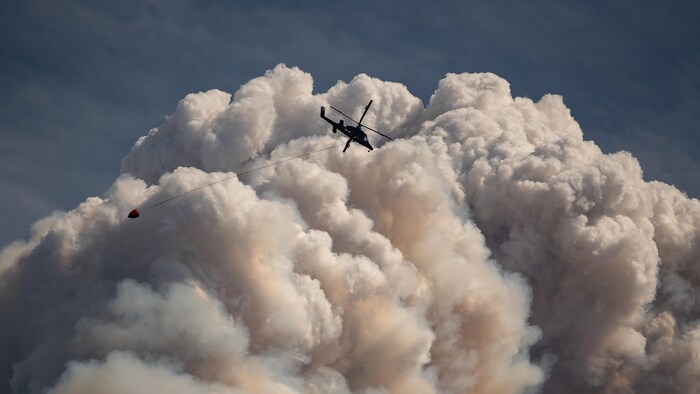 Un hélicoptère survole un immense nuage de fumée.