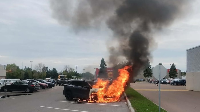 Une voiture en flammes dans un stationnement.