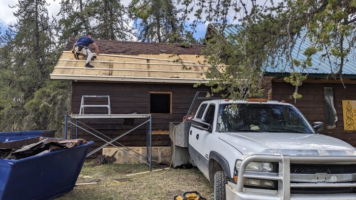 Un ouvrier est sur le toit d'un chalet pour le remplacer.