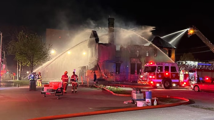 Des pompiers arrosent une maison à moitié détruite par les flammes.