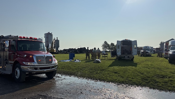 Un camion de pompier, plusieurs pompiers et divers véhicules sont stationnés sur l'herbe.