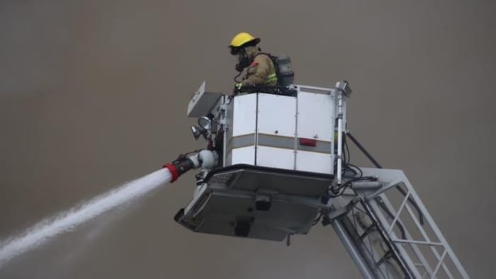 Un pompier, installé dans la nacelle d'un camion-échelle, dirige une lance à eau.