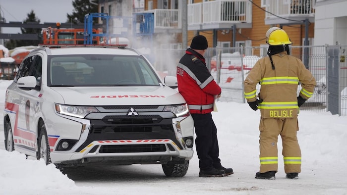 Deux pompiers observent une résidence qui a été la proie des flammes.