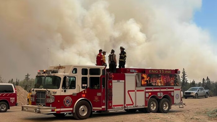 Des pompiers se tiennent sur un camion  près du feu de forêt incontrôlable dans le comté de Shelburne.