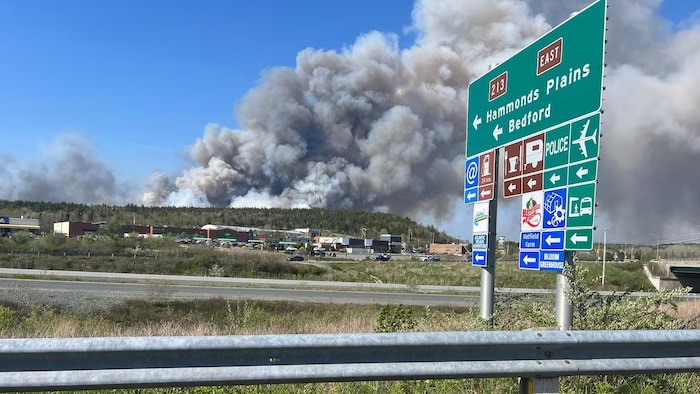 Un panneau routier de la route 213 indiquant la direction d'Hammonds Plains et une épaisse fumée au loin par-dessus une colline.