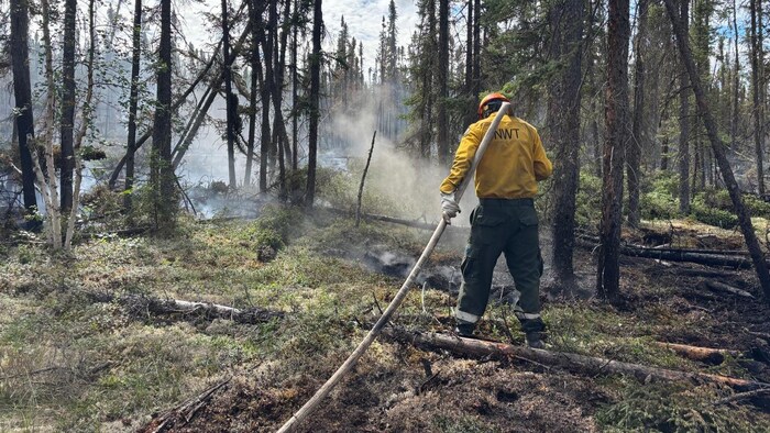 Un pompier forestier arrose le sol près de la communauté de Wrigley le 4 juillet.
