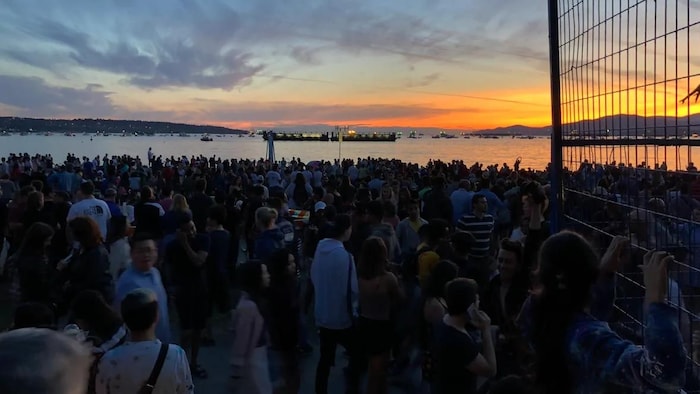 Des centaines de personnes regardent un ciel illuminé au-dessus de l'eau.