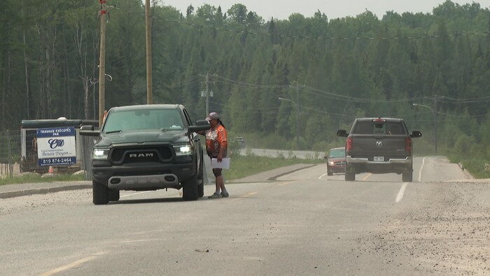 Un homme, debout sur la route, discute avec le conducteur d'une camionnette arrêtée.