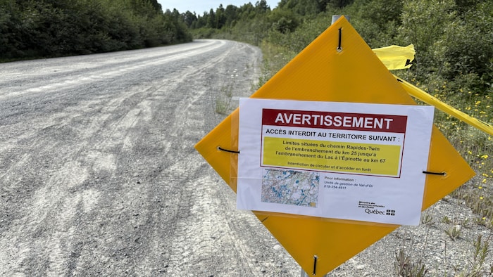 Un écriteau indiquant un avertissement d'accès interdit pour un territoire, au bord d'un chemin en gravier bordé d'arbres.