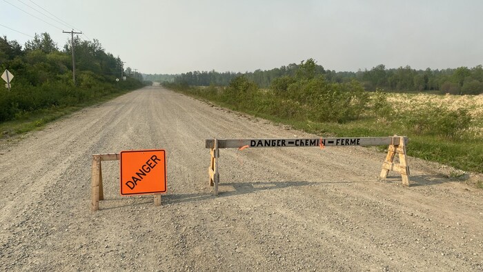 Une affiche indiquant Danger et une barrière indiquant Danger - chemin fermé, sur une petite route en gravier.