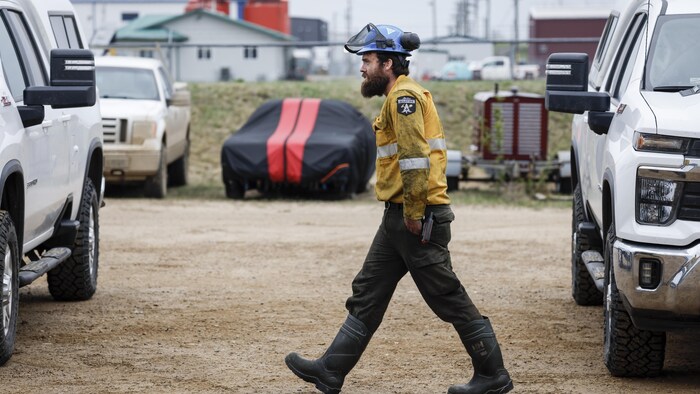 Un pompier forestier marche entre des voitures, recouvert de suie.