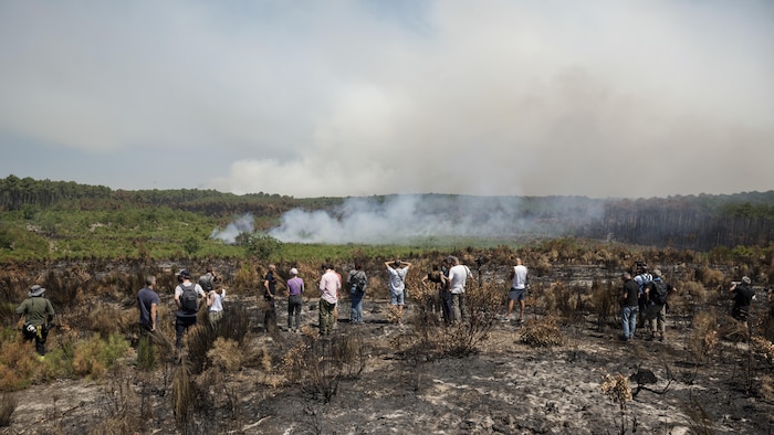 Un groupe de personnes observe de la fumée s'élevant dans le ciel au loin.