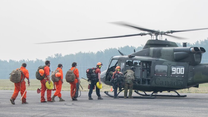 Des soldats et des pompiers civils montent à bord d’un hélicopter.