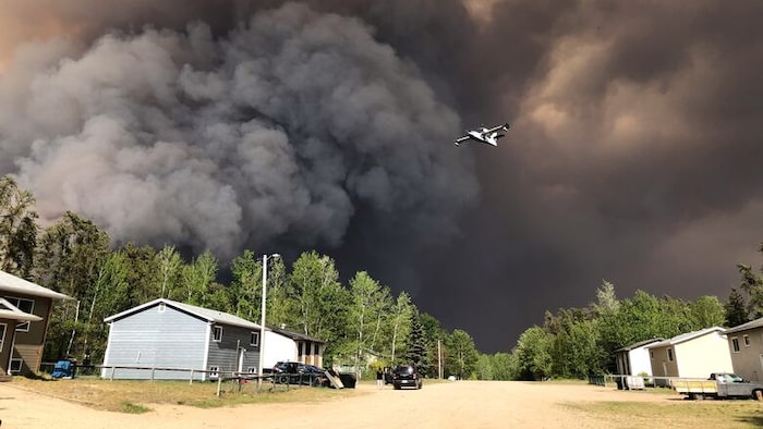 Un avion-citerne vole devant un nuage de fumée noire provenant d'un feu de forêt qui s'élève dans le ciel au-dessus de Weyakwin, en Saskatchewan, le 28 mai 2025.
