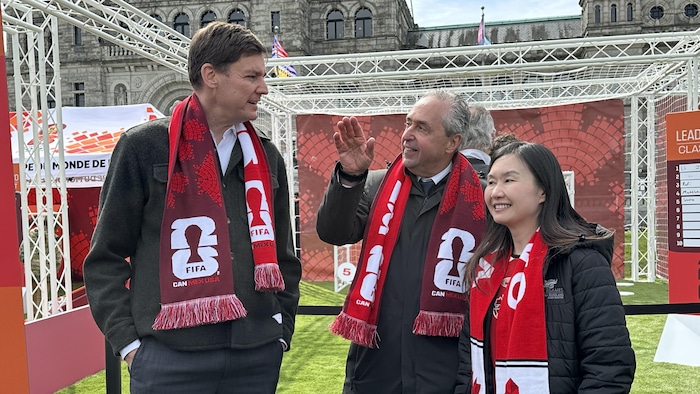 Le premier ministre David Eby, le directeur général du tournoi pour le Canada Peter Montopoli et la ministre du Tourisme Anne Kang. Ils portent des écharpes de la FIFA.