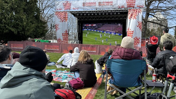 Des personnes regardent un match de soccer diffusé sur un grand écran.