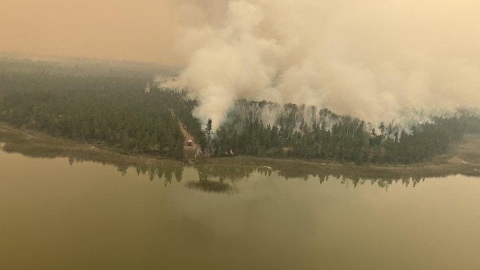 Un cours d'eau en premier plan, et de la fumée émanant de la forêt sur la berge, l'image étant nappée d'un voile de fumée verdâtre. 