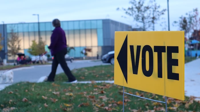 Une personne se dirige vers un bâtiment dans la direction vers laquelle une affiche indiquant « Vote » pointe.