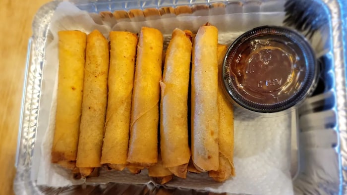Nasa aluminum container ang mga lumpia katabi ang sauce.
