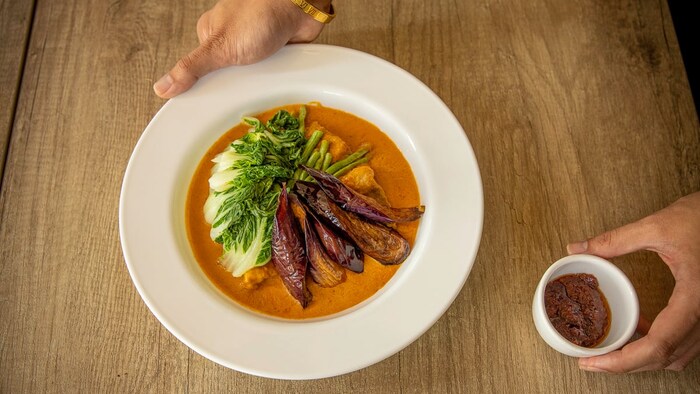 Beef kare-kare na nasa plato katabi ang maliit na lalagyan na may bagoong.