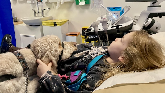 Une fille de six ans couchée dans un lit d'hôpital avec un chien d'assistance.