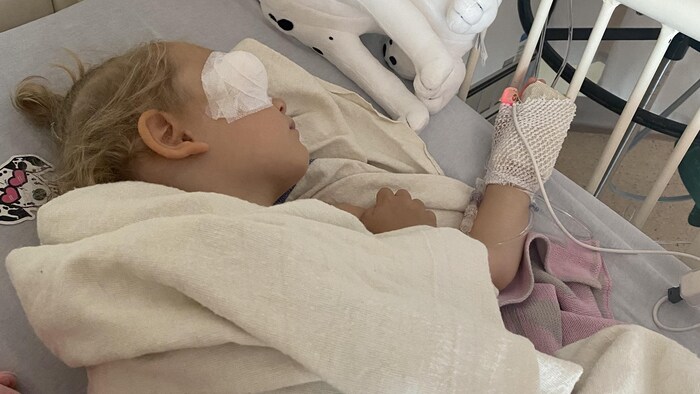 Une jeune fille allongée sur un lit d'hôpital, un bandage recouvrant son œil droit.