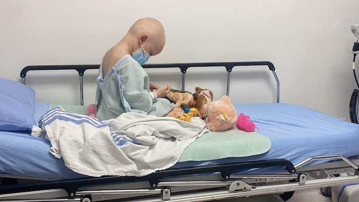 Une jeune fille chauve assise sur un lit d’hôpital.