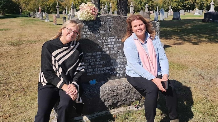 Les deux femmes sont assises devant une pierre tombale dans un cimetière.