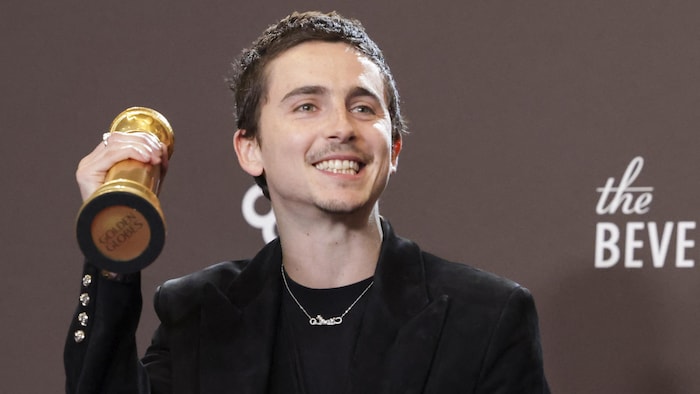 Il tient son trophée dans la main droite.