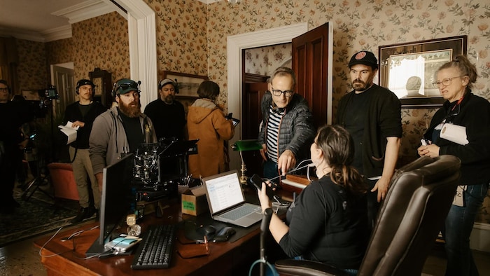 Phil Comeau est entouré de plusieurs membres de son équipe. Il parle à une dame assise à un bureau.