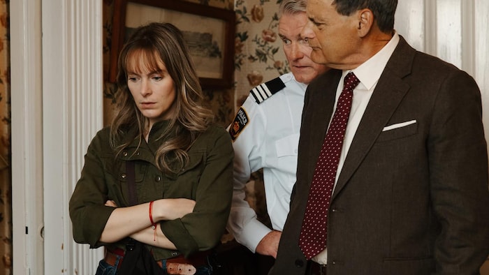 Tanya Brideau se tient debout, les bras croisés, près des personnages d'un policier et d'un détective dans une scène du film.