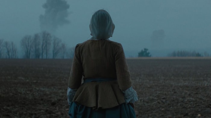 Une femme vêtue d'un costume d'époque est debout dans un champ à l'aube.