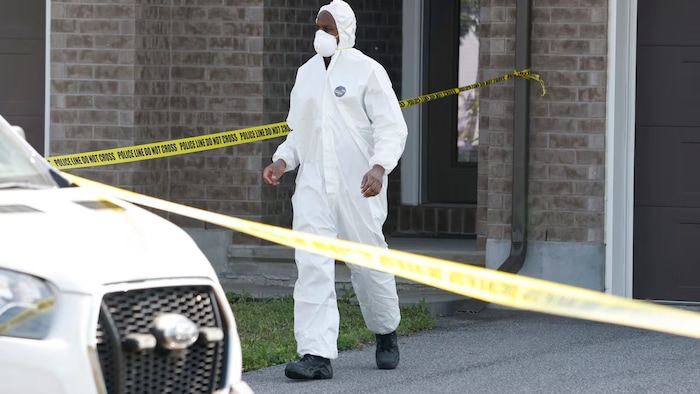 Une personne porte de l'équipement de protection alors qu'elle quitte la maison du quartier Findlay Creek, où il y a un périmètre de sécurité.