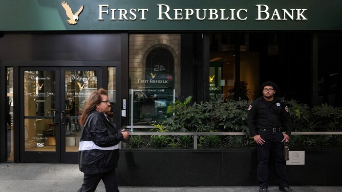 Une passante marche devant un garde de sécurité à l'extérieur d'une succursale de la First Republic Bank.