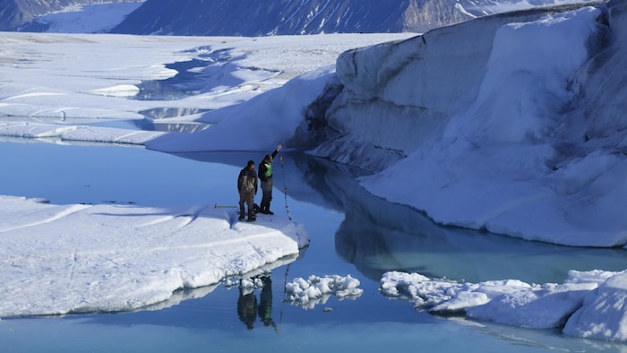 Deux personnes sur le bord d'une plateforme de glace plongent des instruments dans l'eau.