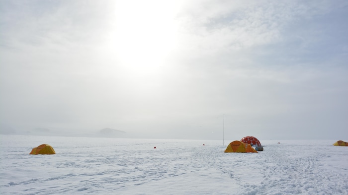 Quelques tentes sur une immense couche de glace qui s'étend à l'infini.