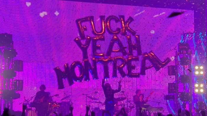 Un groupe joue sur une scène devant une foule. Au-dessus d'eux, des ballons en forme de lettres qui épellent : Fuck Yeah Montreal.
