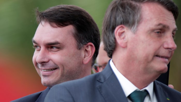 Flavio Bolsonaro, souriant, se tient derrière Jair Bolsonaro.