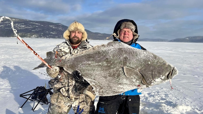 Deux pêcheurs tiennent un énorme poisson sur les glaces.