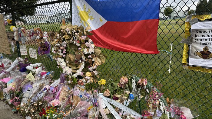 Des fleurs et des couronnes, déposées près d'une clôture, en dessous du drapeau philippin.