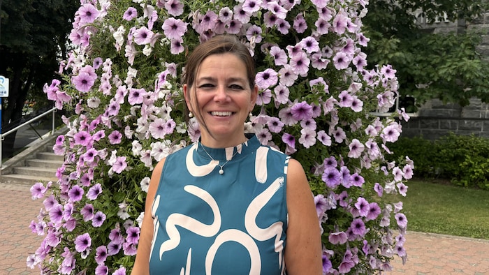 Bianka Villeneuve sourit devant une talle de fleurs roses.
