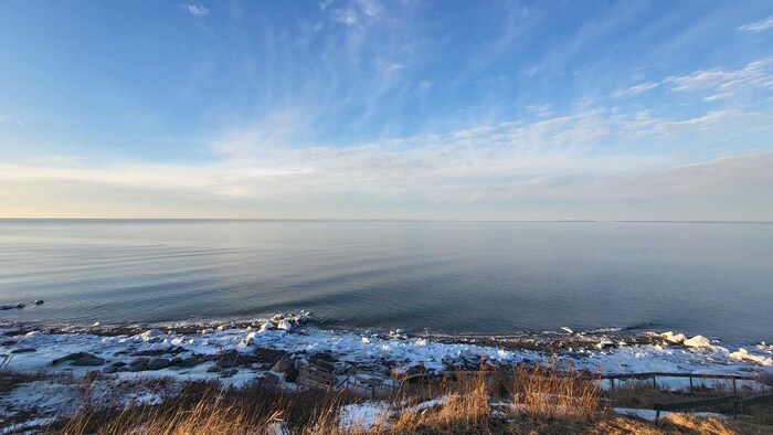 Une vaste étendue d'eau bleue. Il s'agit du fleuve Saint-Laurent, sans glace, mais de la neige recouvre la plage uniquement. 