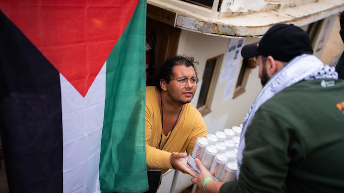 Des personnes chargent des provisions à bord d'un bateau, orné d'un drapeau palestinien.