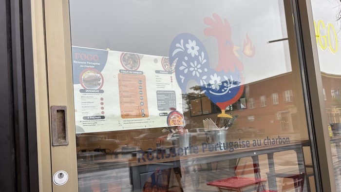La vitrine d'un restaurant sur laquelle on peut voir un coq ornementé qui crache une flamme. 