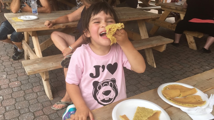 Une petite fille mange une ploye à la Foire brayonne.
