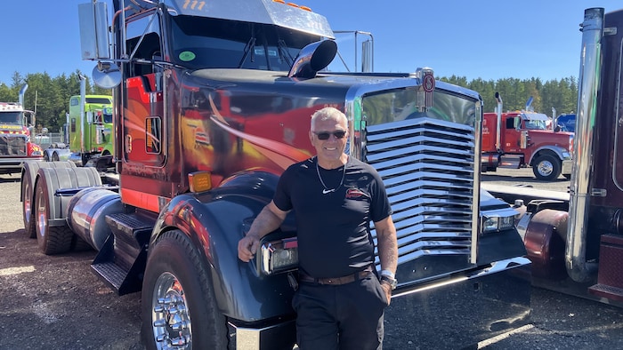 Yvon Vigneault sourit à la caméra en prenant la pose, un bras accoté sur son camion.